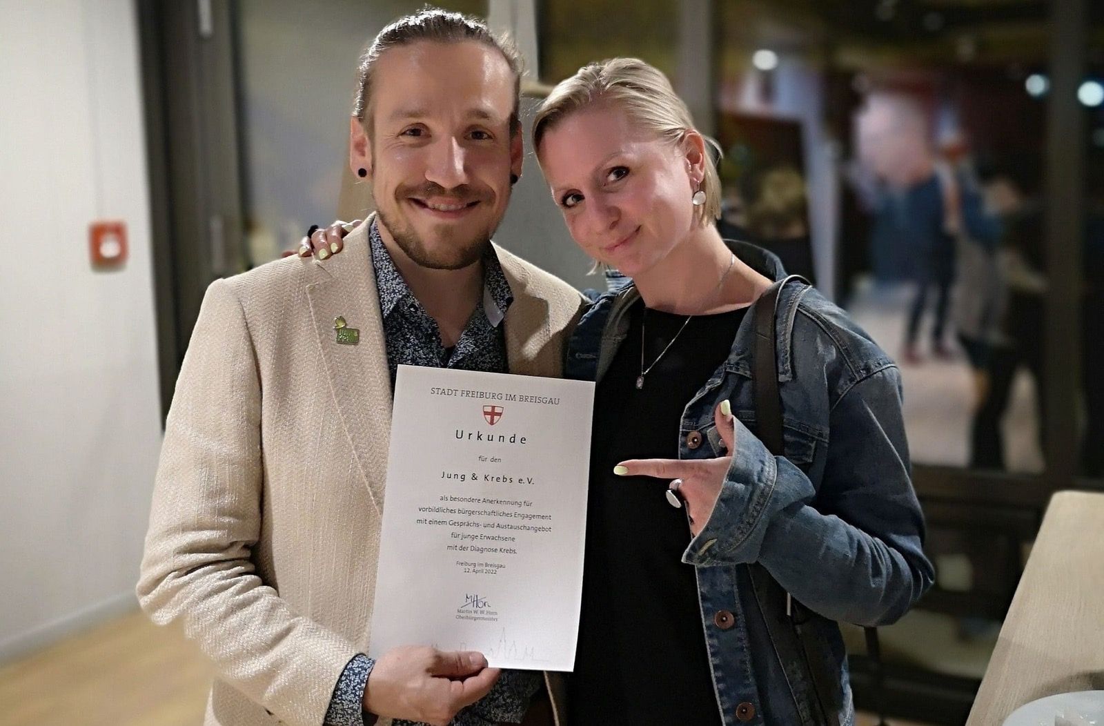 Carsten und eine Frau halten lächelnd eine Urkunde der Stadt Freiburg für Jung und Krebs e.V.