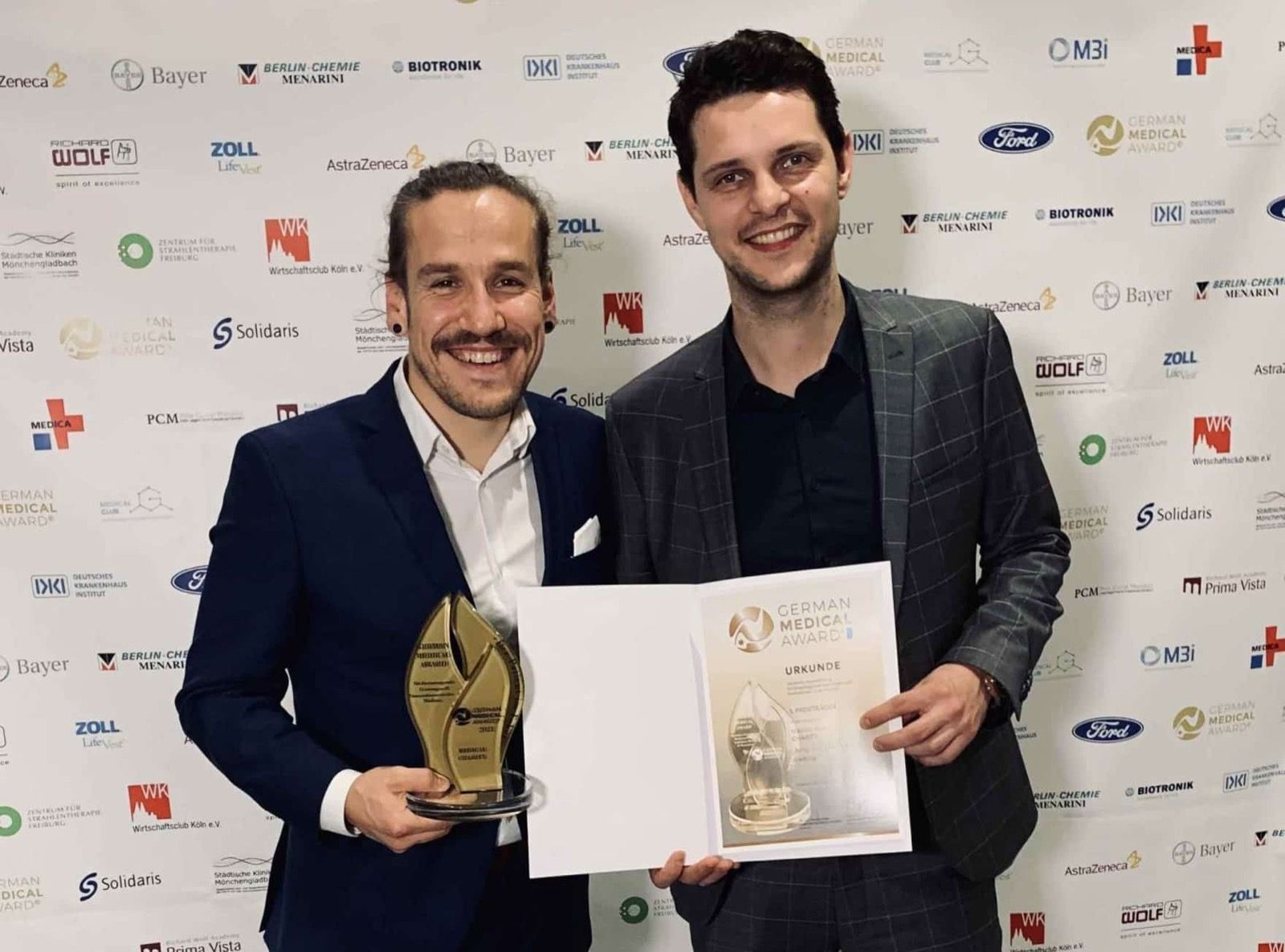 Carsten mit Trophäe und ein Mann mit Urkunde vor der Pressewand des German Medical Award.