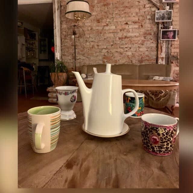 Eine weiße Teekanne und bunte Tassen auf einem Holztisch im Café Metamorphose in Rheinfelden.