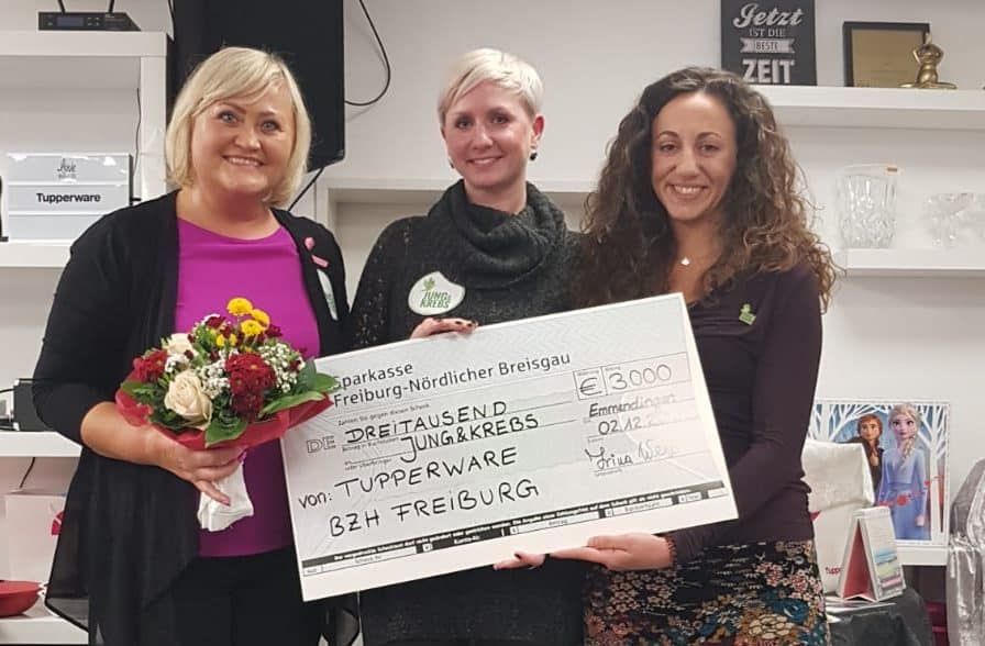 Drei Frauen mit Blumenstrauß halten einen Spendenscheck von Tupperware-Vertreterinnen über 3.000 Euro.