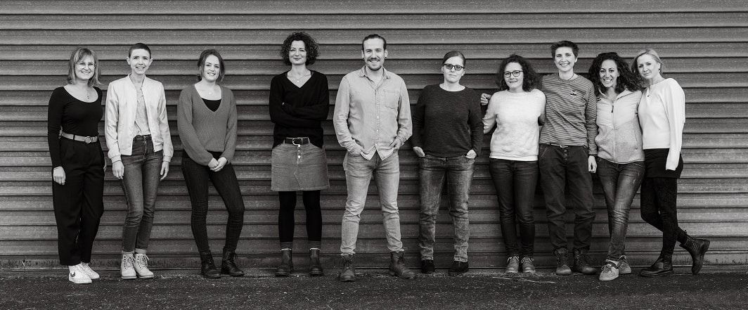 Zwölf Menschen aus dem Verein stehen nebeneinander vor einer Wand, Schwarz-Weiß-Foto.