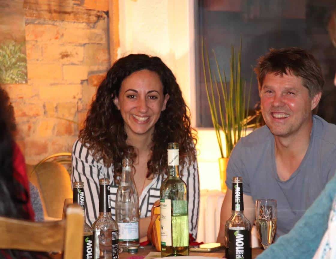 Eine junge Frau und ein Mann sitzen nebeneinander an einem Tisch und lächeln in die Kamera.